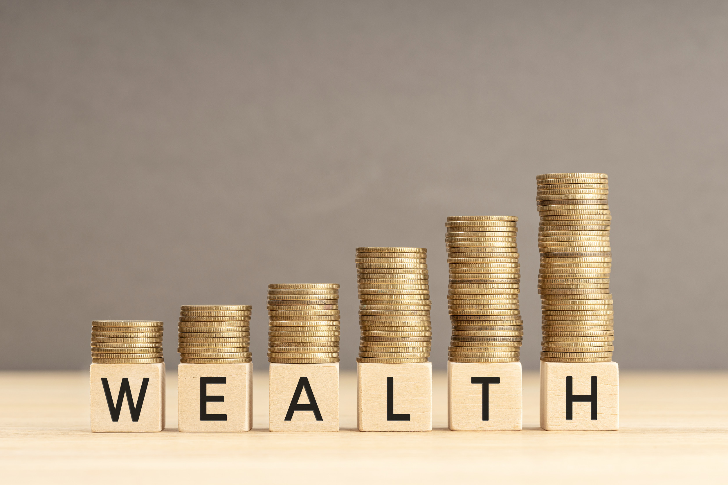 Wealth word in wooden blocks with coins stacked in increasing stacks Wealth increasing concept Copy space