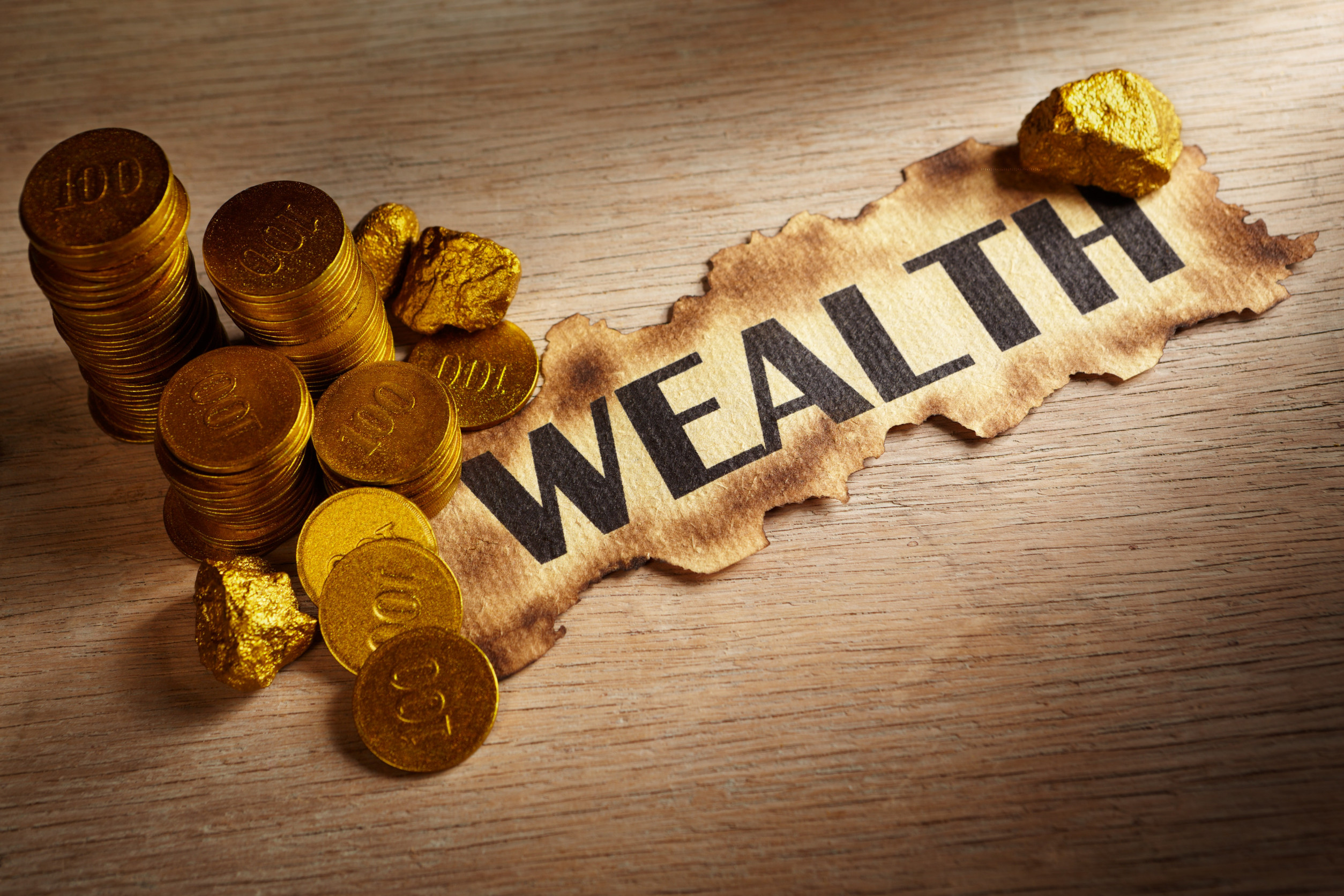 Wealth written on vintage paper and stack of gold coins and gold rocks